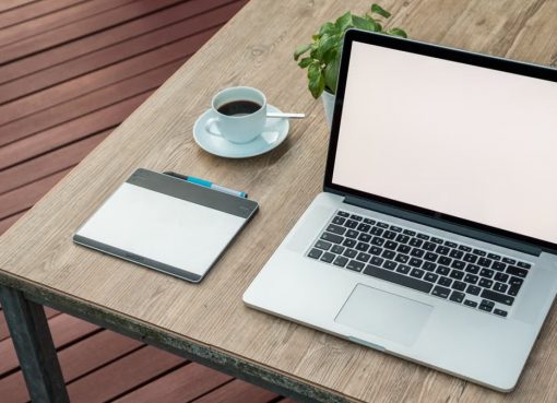 A minimalist outdoor workstation with laptop, coffee, and tablet on a rustic table.